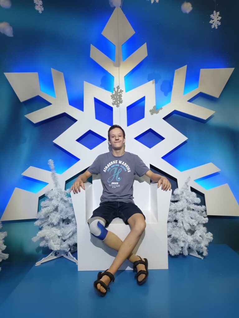 Chłopiec siedzący na białym fotelu imitującym tron, a za jego plecami niebieskie tło i dekoracje w kształcie dużych śnieżynek 
