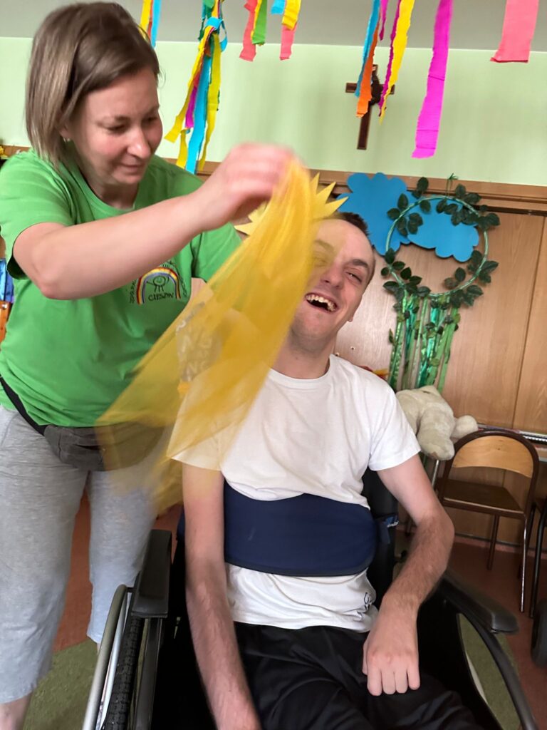 roześmiany chłopak na wózku. Obok kobieta machająca żółtą chustką. 
