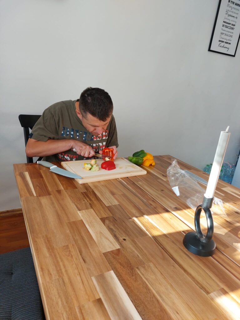 Chłopak siedzący przy stole i krojący paprykę 
