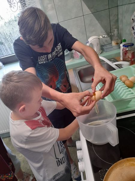 Dwóch chłopaków w kuchni podczas rozbijania jajek do miski 