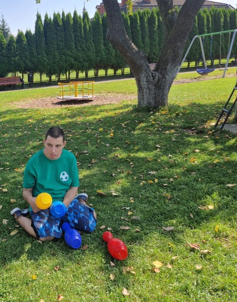 Chłopak siedzący na trawie bawi się kręglami 