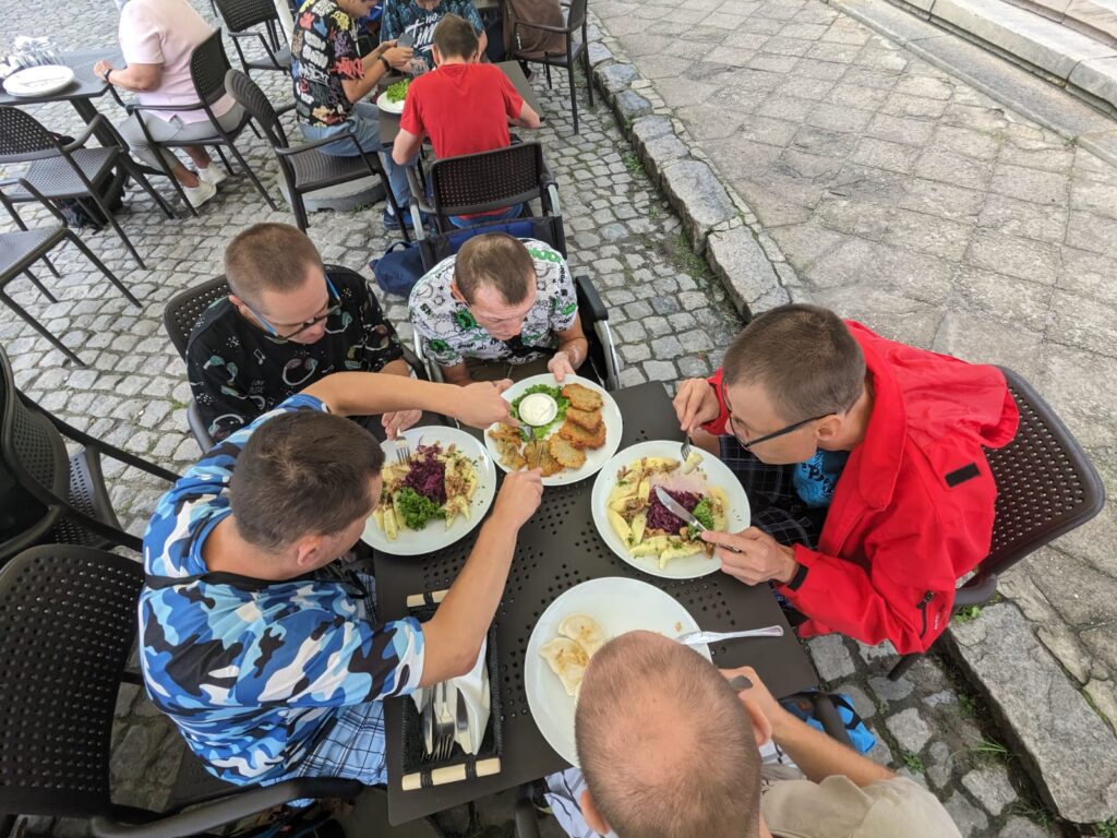 Grupa wokół stołu. Przed każdym z chłopaków talerz z daniem obiadowym. 