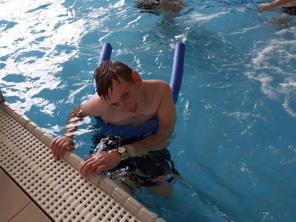 chłopiec pływający z "makaronem" przy brzegu basenu. 