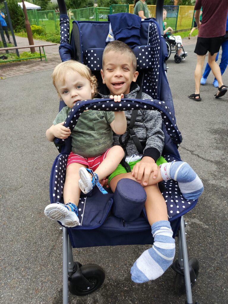 Dwóch małych chłopców siedzących w jednym wózku spacerowym  