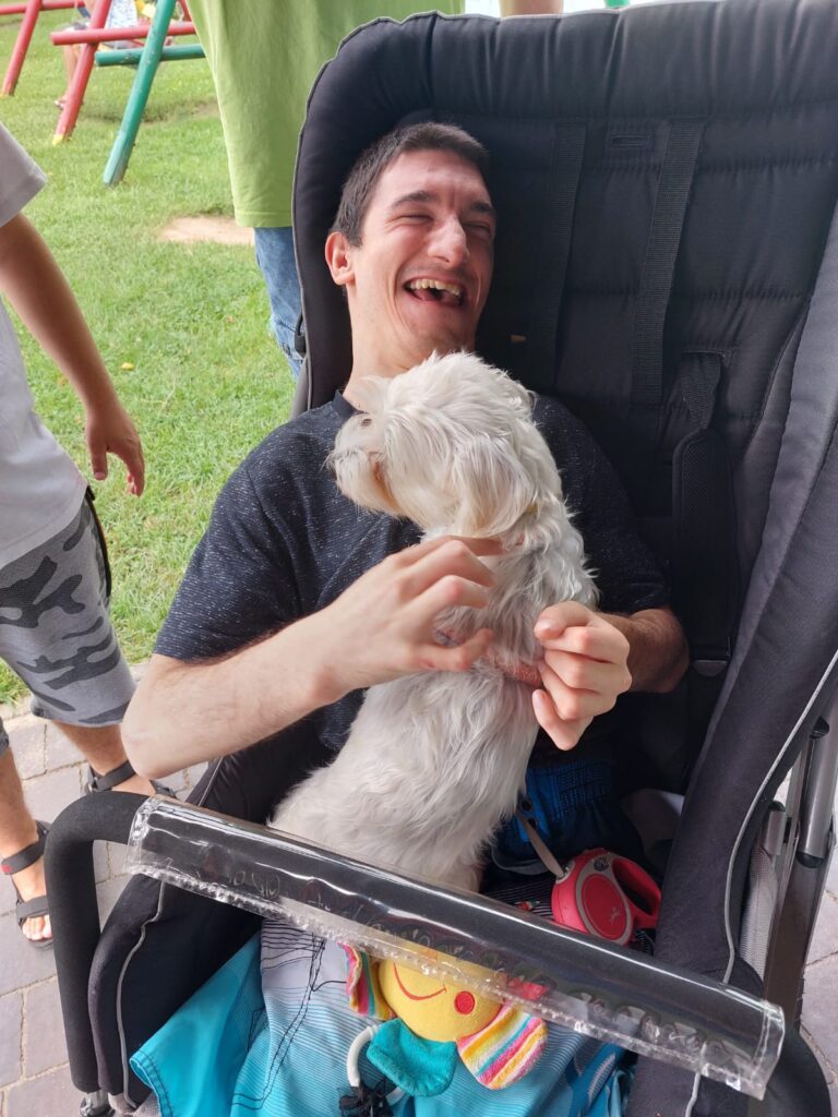 Chłopiec siedzący w wózku. Na kolanach trzyma małego psa. 
