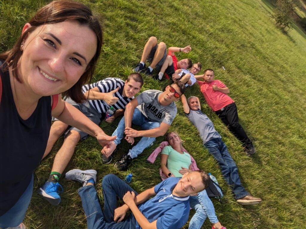 Kobieta robi zdjęcie selfie z gruupą chłopaków leżących na trawie 