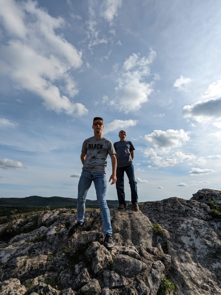 Dwóch mężczyzn stoi na skałach. Za nimi niebo pełne małych chmur 