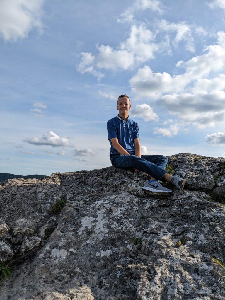 Chłopak siedzący na skale. Za nim niebo i chmury 