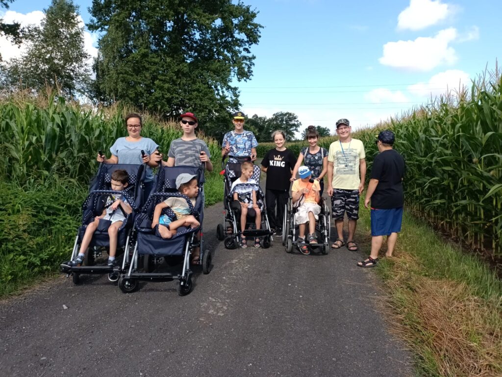 zdjęcie grupowe podczas spaceru. Grupa stoi na polnej drodze. Po obu stronach rośnie kukurydza. 