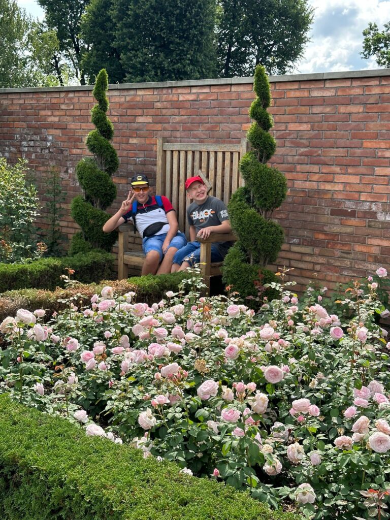 Chłopcy siedzący na ławce. Przed nimi ogród różany 