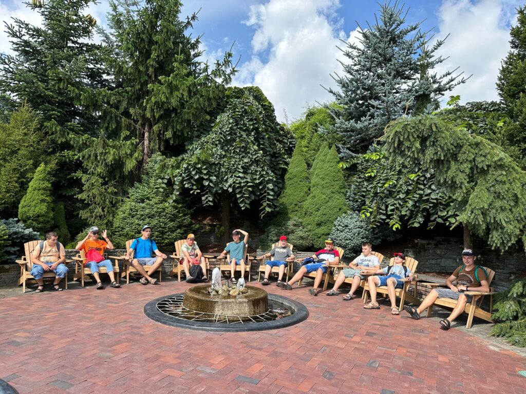 Grupa osób siedząca na leżakach wokół fontanny 