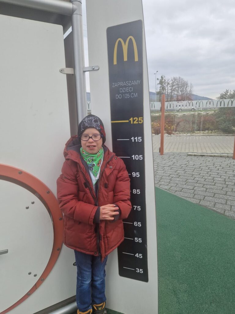 Chłopiec stoi przy wejściu do zjeżdżalni i mierzy swój wzrost przy miarce, która wskazuje 125 cm. 