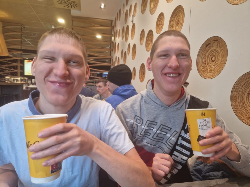 Dwóch uśmiechniętych chłopaków bliźniaków siedzą przy stole w restauracji i piją napój. 