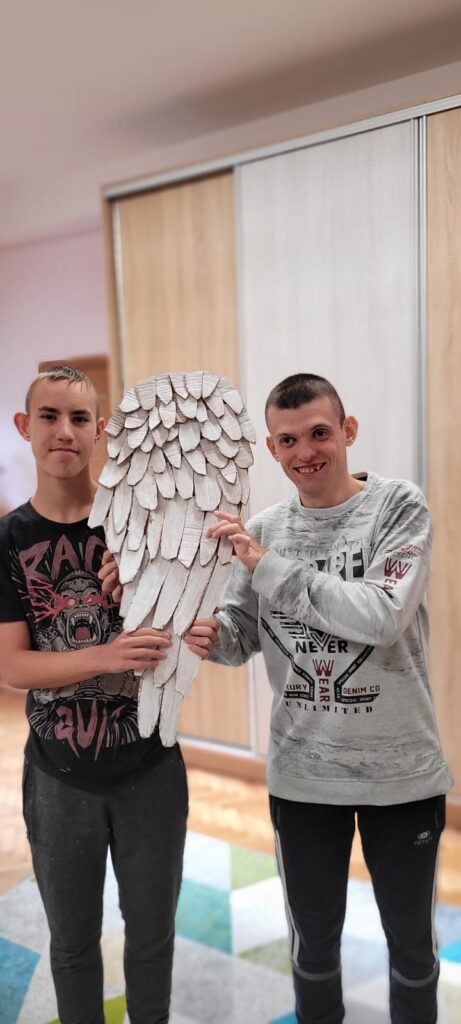 Dwóje chłopaków pokazujących wykonane przez siebie skrzydło anioła. 