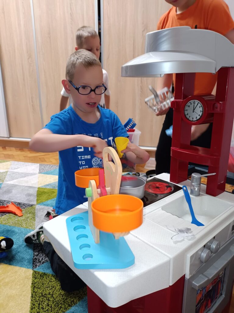 Chłopiec bawiący się przy zabawkowym aneksie kuchennym 