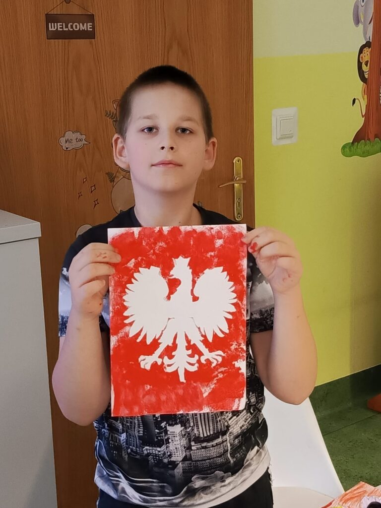 Chłopiec prezentujący swoją pracę plastyczną z godłem Polski. 