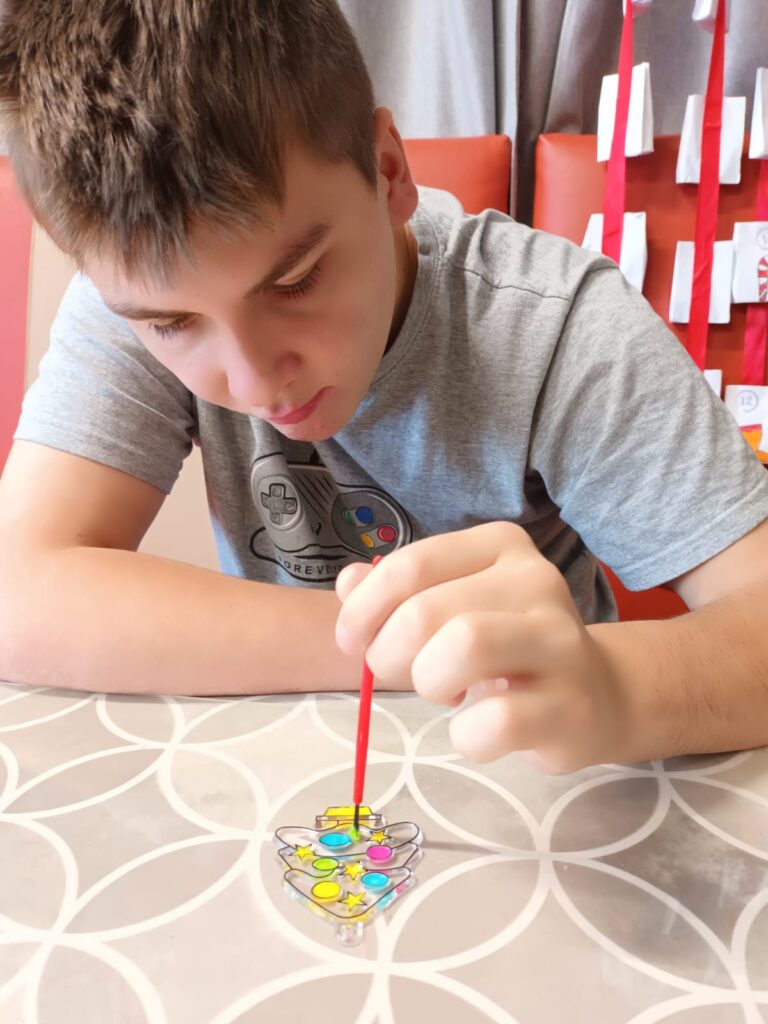 Chłopiec przy stole malujący farbami przezroczyste ozdoby świąteczne 