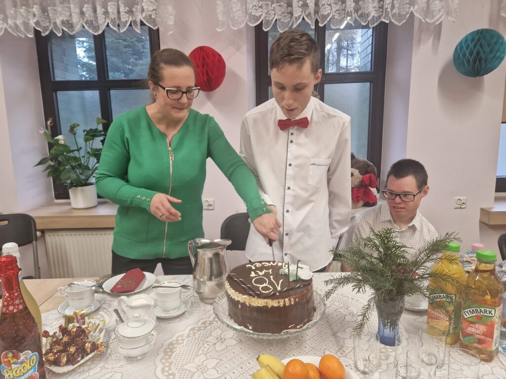 Kobieta pomaga chłopakowi kroić tort. 