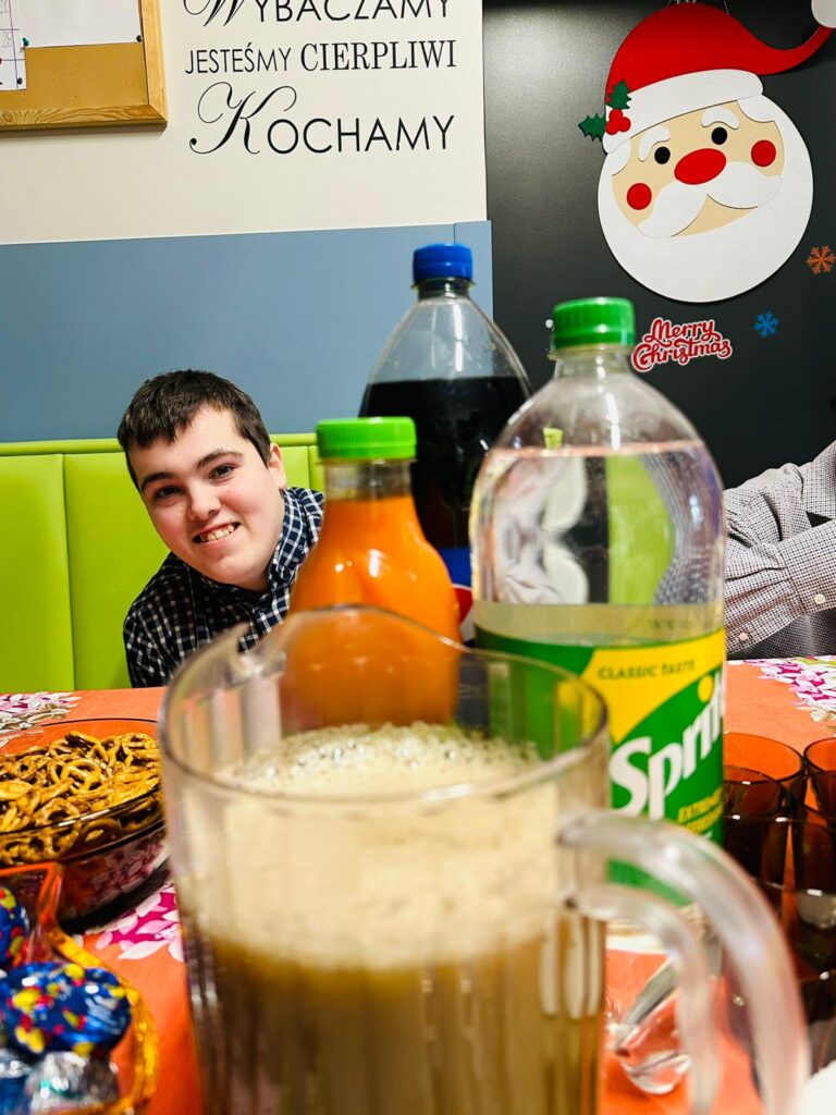 Chłopak siedzący za stołem i wychylający się zza butelek z napojami. 