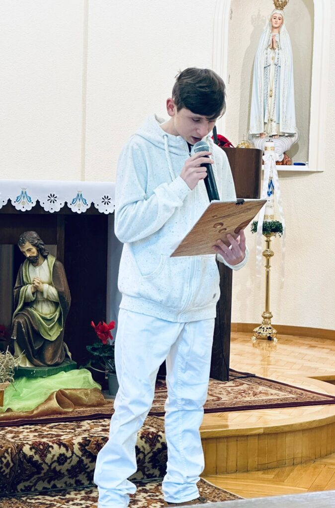 Chłopiec ubrany na biało czytający do mikrofonu. 