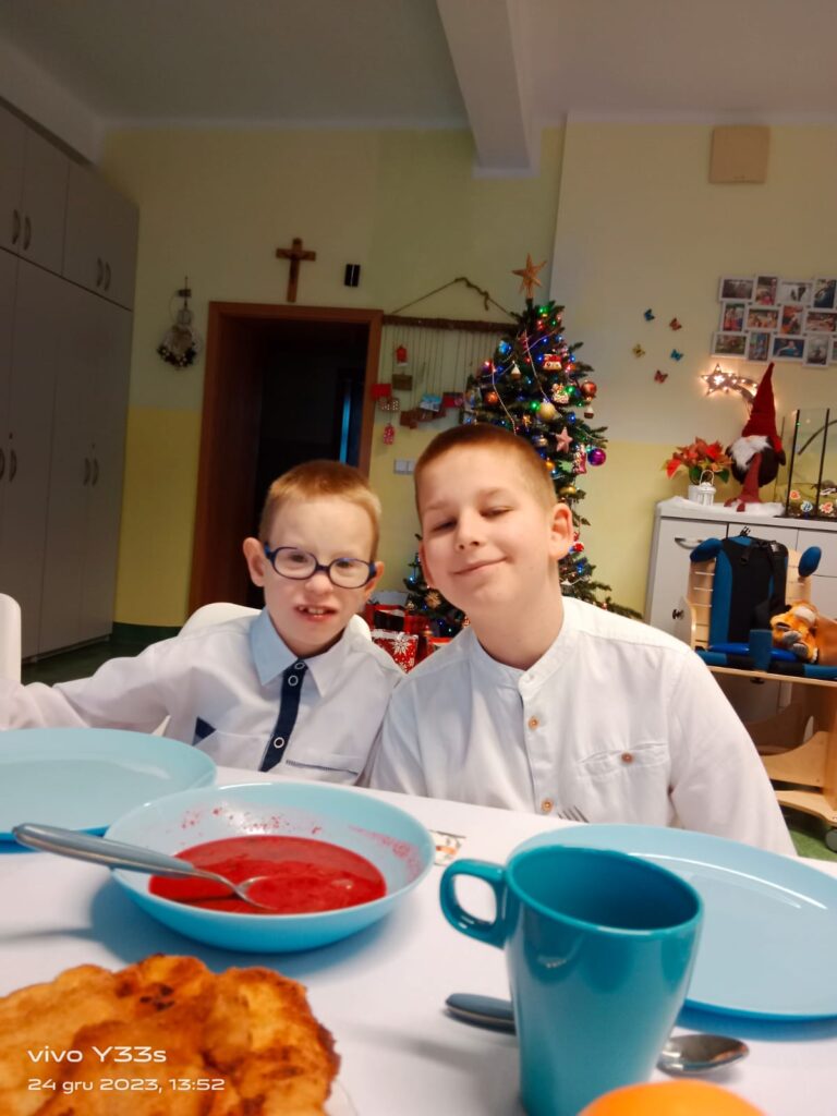 dwaj chłopcy w białych koszulach pozują do zdjęcia za zastawionym stołem. 
