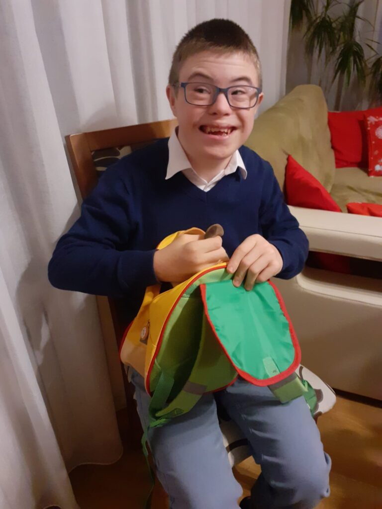 Uśmiechnięty chłopczyk wyciąga coś z kolorowego plecaczka. 