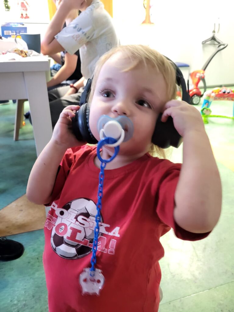 Mały chłopczyk ze smoczkiem w ustach i wielkimi słuchawkami na uszach. 