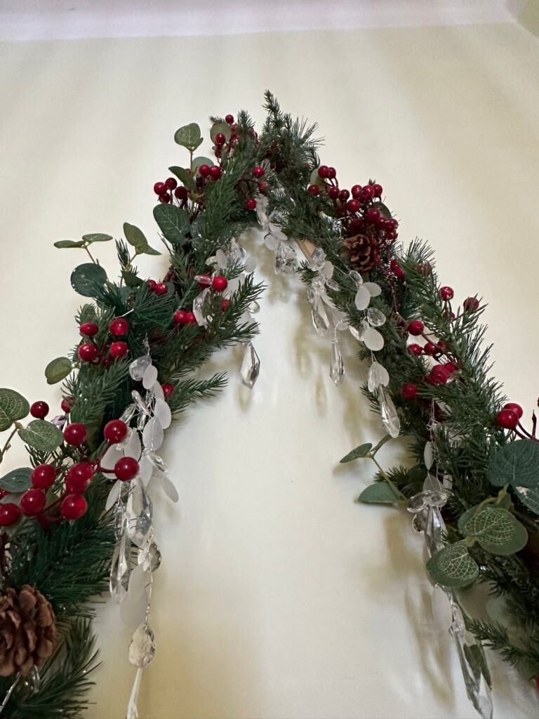 Dekoracja świąteczna: Płaska choinka na ścianie zrobiona z zielonego łańcucha, ozdobiona diamencikami, szyszkami i jarzębiną. 