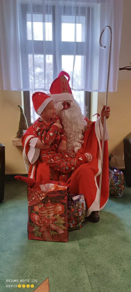 Mężczyzna w "Biskupim" stroju św. Mikołaja wręcza paczkę z prezentem jednemu z chłopaków. 