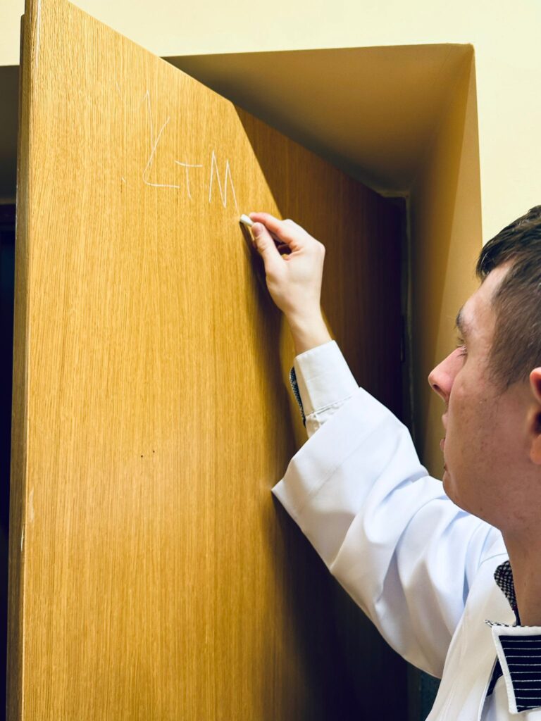 Chłopak w białej komeszce pisze kredą na drzwiach "K+M+B" 