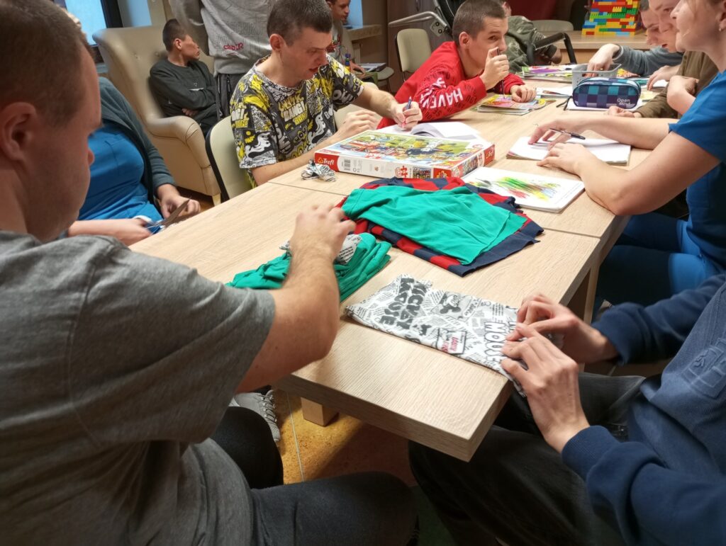 Chłopcy przy stole składający ubrania. Obok inni chłopcy układający puzzle. 