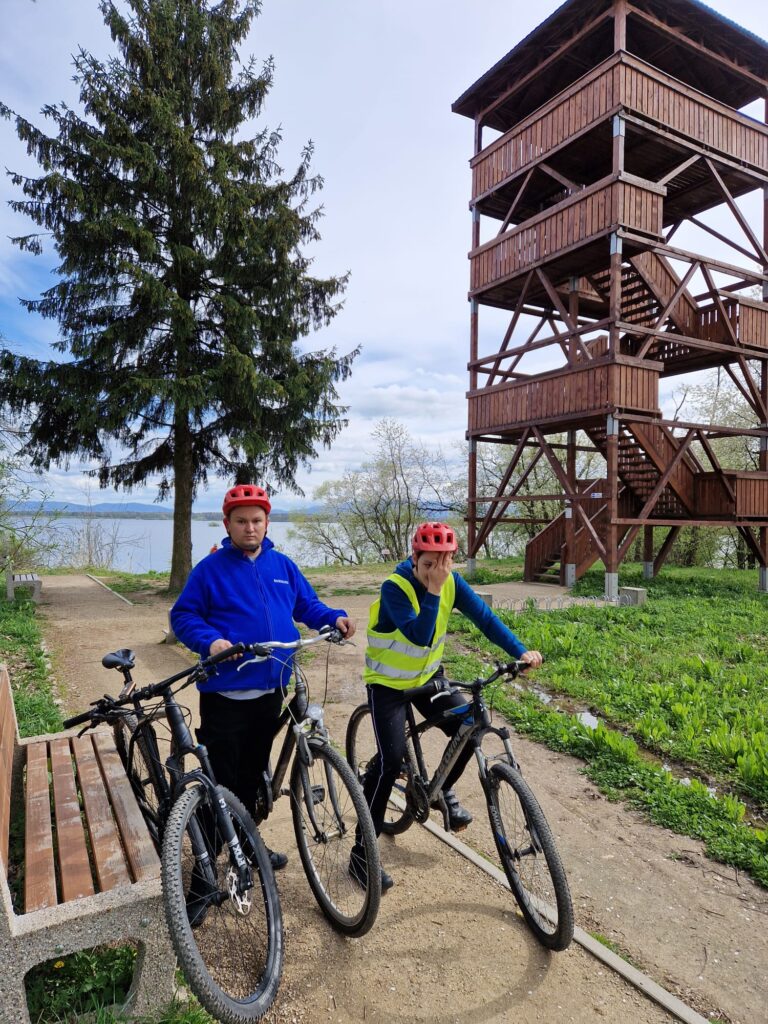 Dwóch chłopaków stoi przed drewnianą wieżą. Obok nich rowery. 
