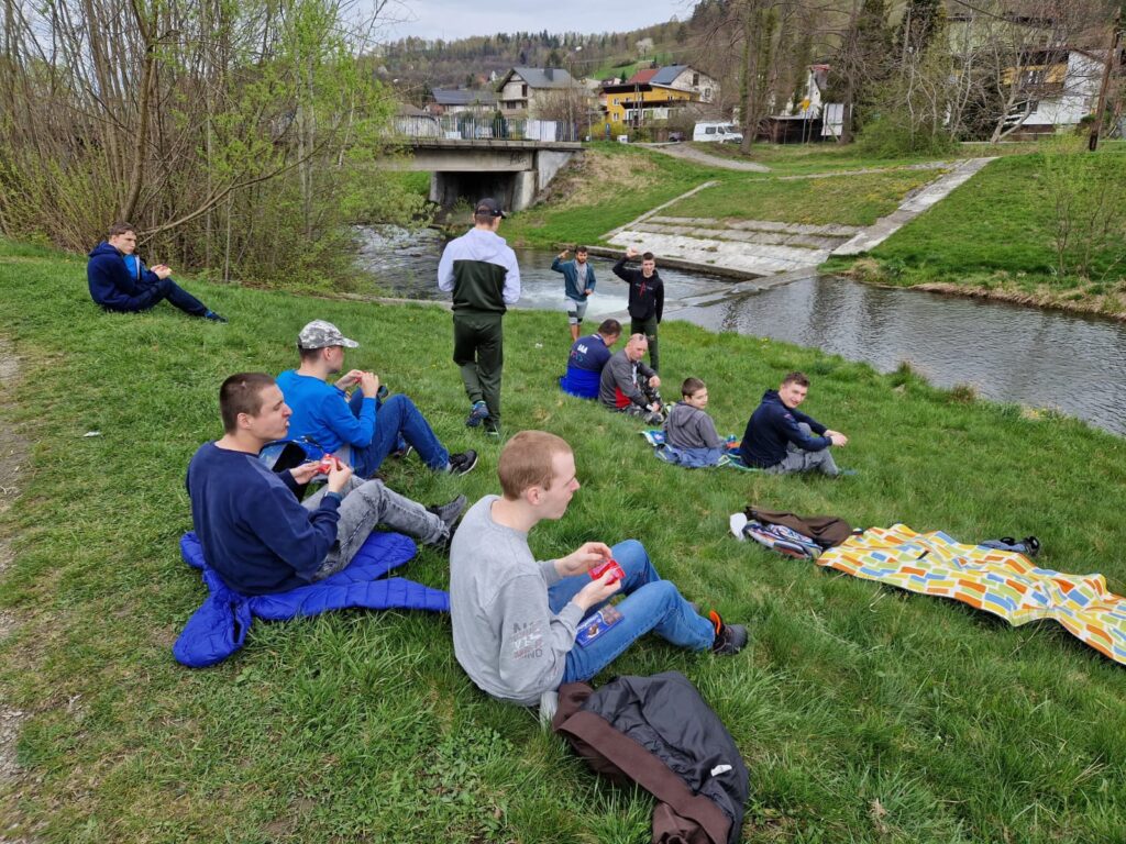 grupa osób siedząca na trawie nad rzeką 