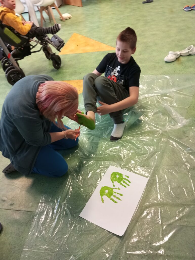 Kobieta malująca chłopcu stopę zieloną farbą. 