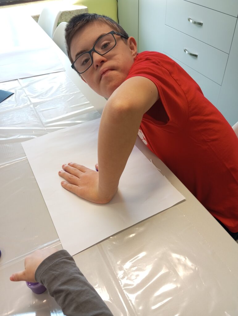Chłopiec odbijający swoją pomalowaną farbą dłoń na kartce papieru. 