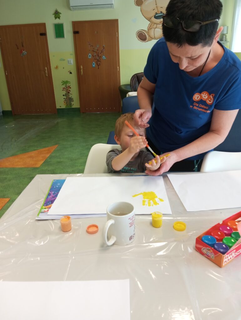 Kobieta pomagająca chłopcu pomalować swoją dłoń farbą. 