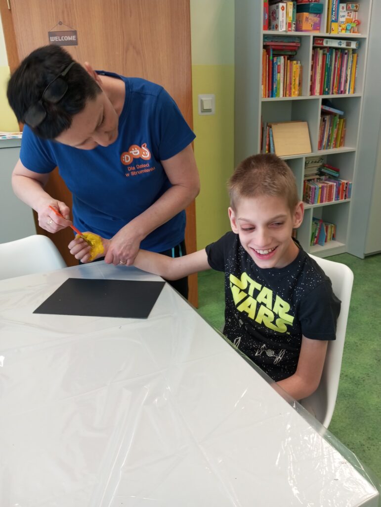 Kobieta pomagająca chłopcu pomalować swoją dłoń farbą. 