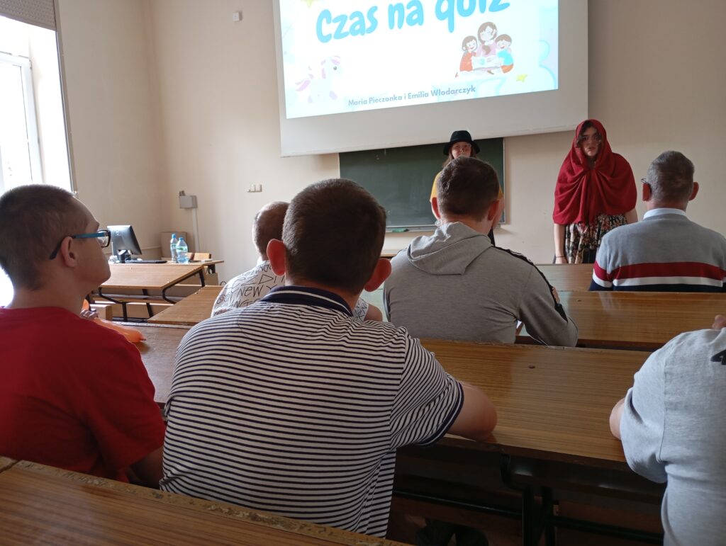 Grupa osób siedząca w klasie. Przed nimi prowadzący zajęcia i wyświetlony napis na ekranie "czas na quiz". 